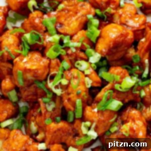 A plate piled high with crispy Bbq Cauliflower Wings, coated in a sticky, savory BBQ sauce, garnished with fresh herbs.