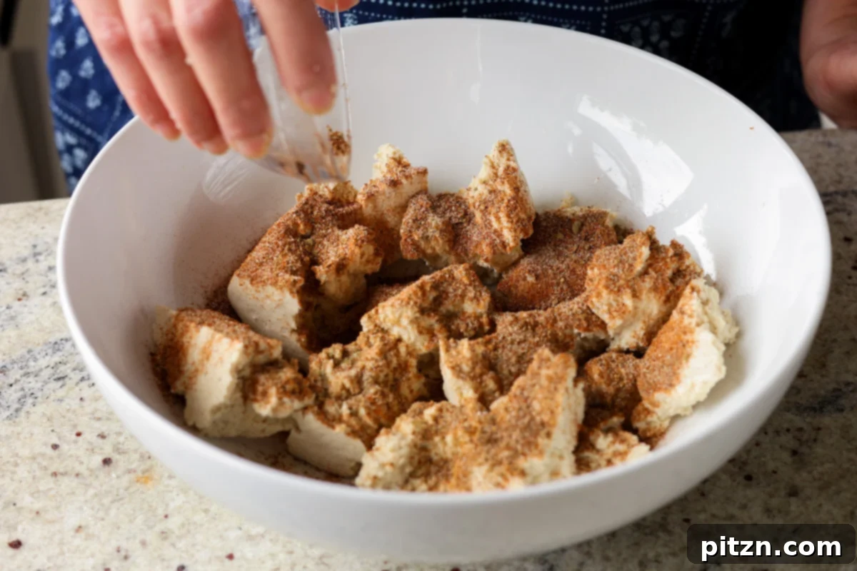 One Pan Chicken Style Braised Tofu and Vegetables 11 Adding a generous amount of the prepared spice rub to the torn tofu pieces in a mixing bowl.