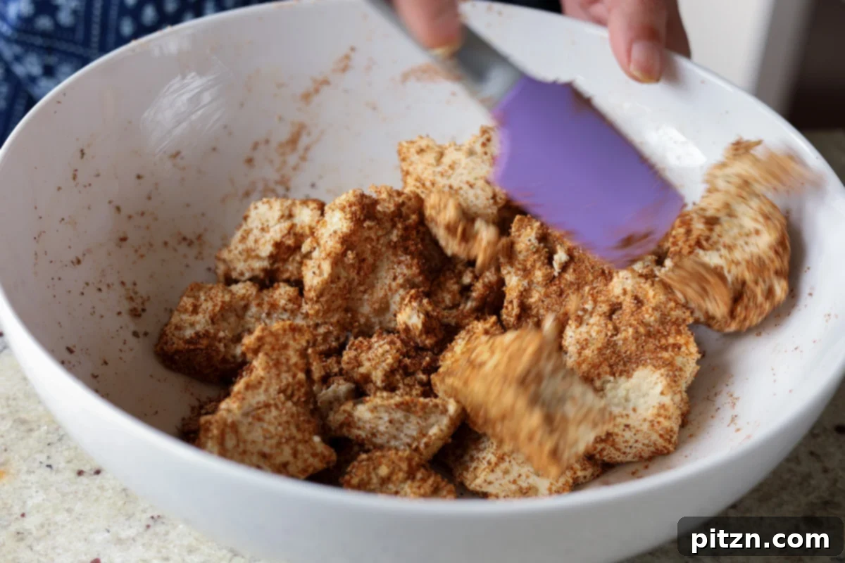 One Pan Chicken Style Braised Tofu and Vegetables 12 Tofu pieces being tossed vigorously in a bowl to evenly distribute the spice rub, showing the uniform coating.