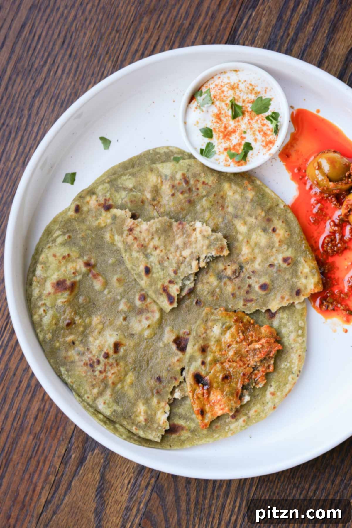Yeast-Free Spinach Paratha Flatbread 2 Spinach Paratha served on a plate with refreshing raita and a tangy Indian pickle, highlighting its vibrant green color.