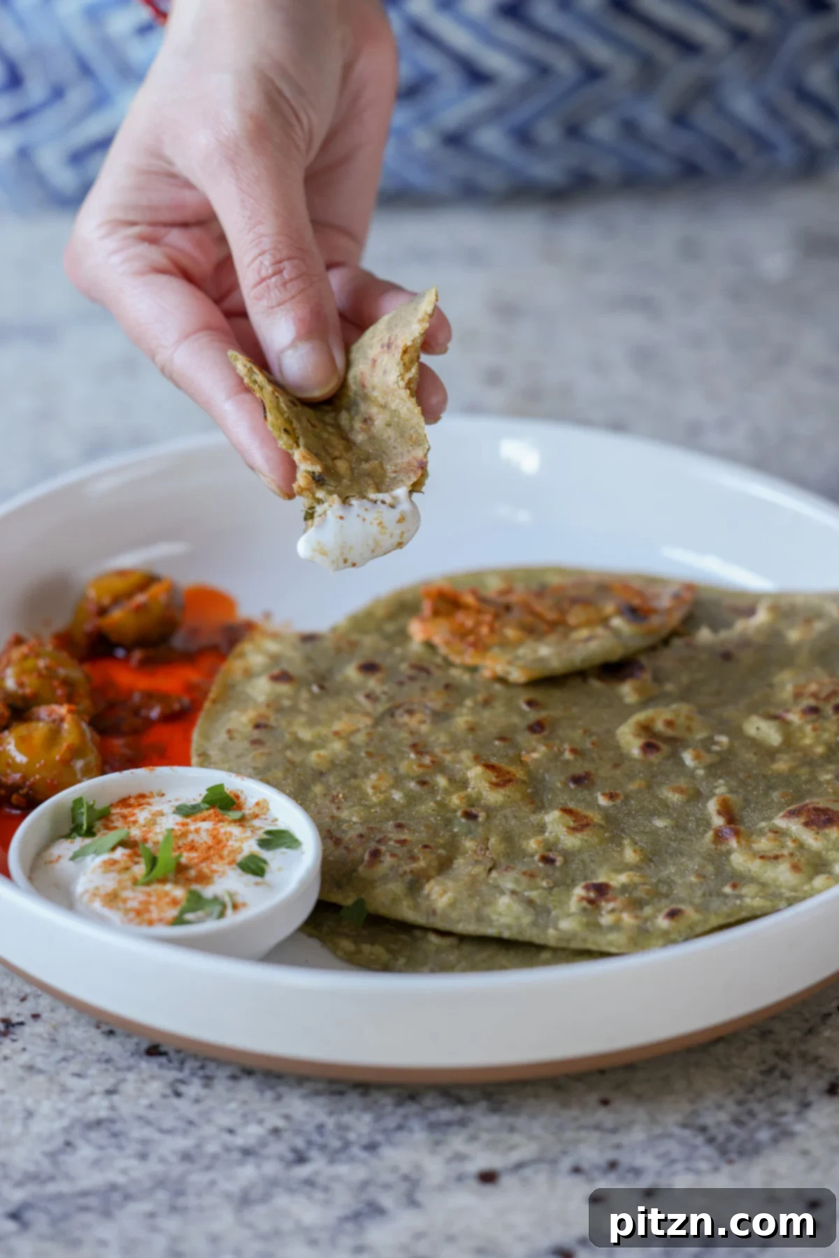 Yeast-Free Spinach Paratha Flatbread 4 A hand gracefully dipping a piece of spinach paratha into a bowl of creamy raita, highlighting a classic pairing.