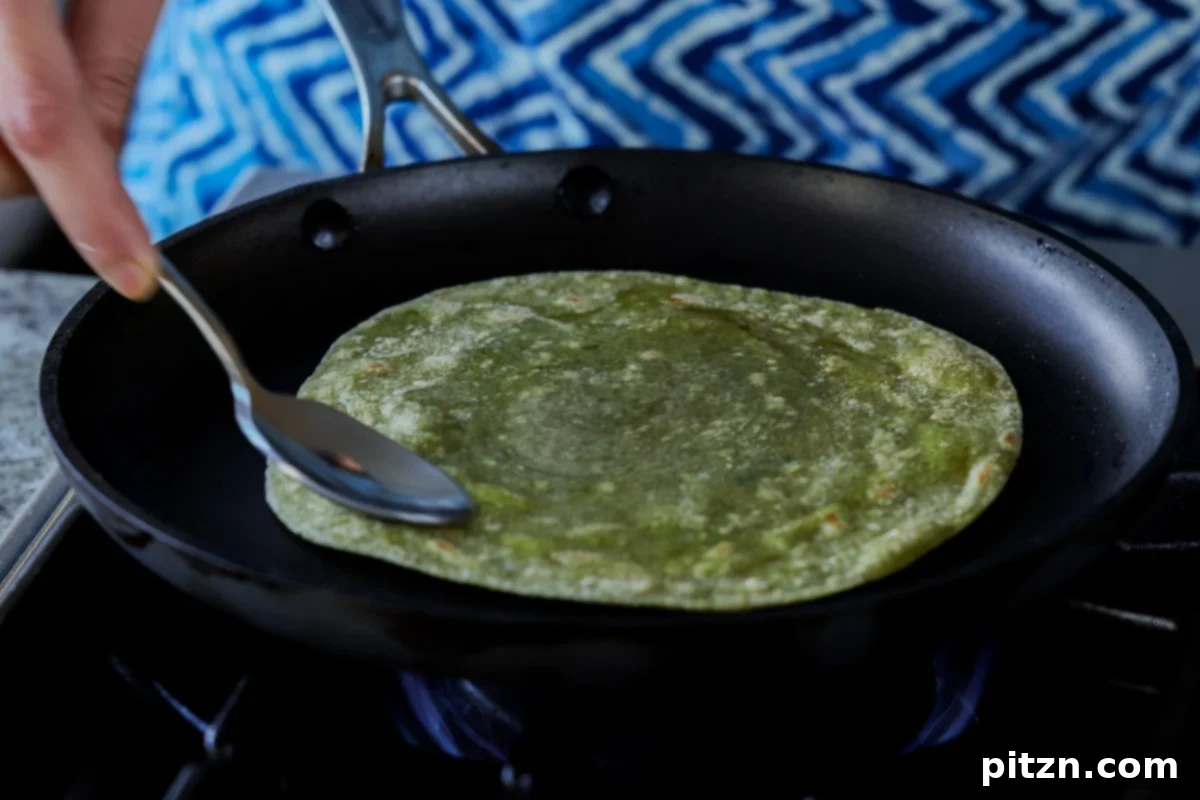 Yeast-Free Spinach Paratha Flatbread 36 Using a spoon to gently press the spinach paratha on the skillet, encouraging even cooking and browning.