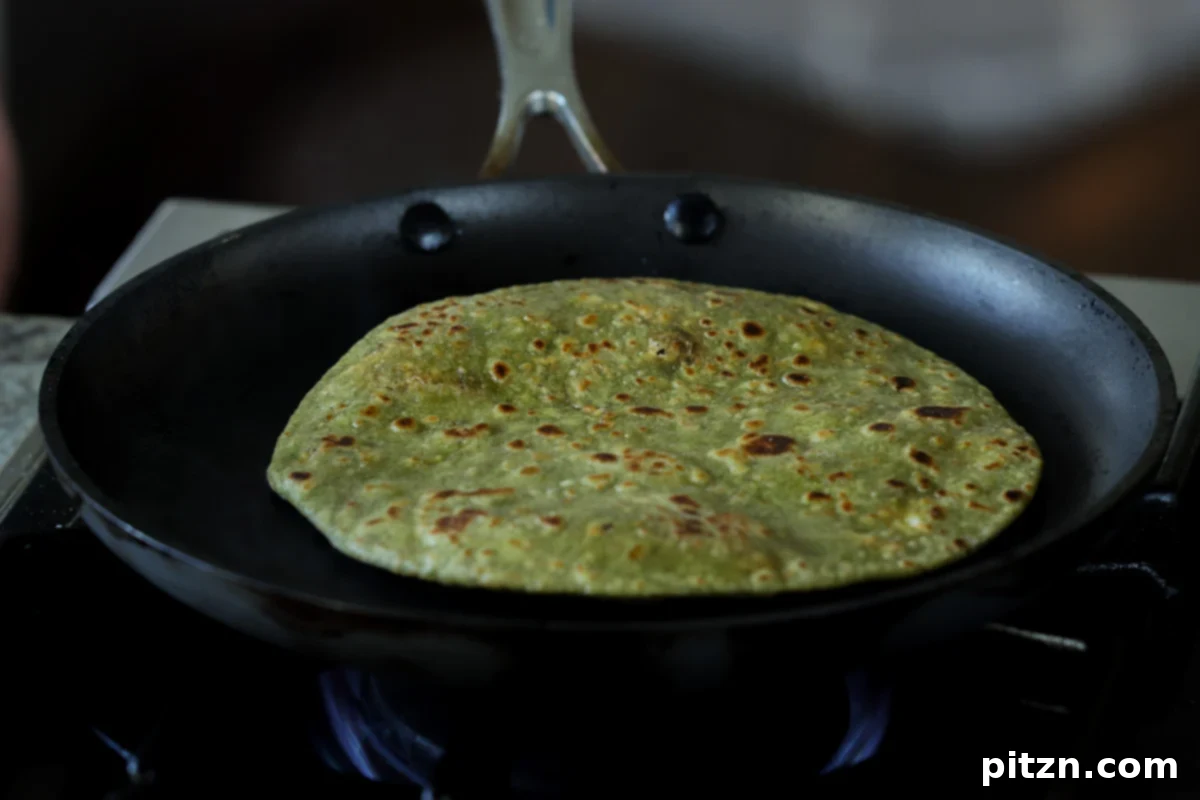 Yeast-Free Spinach Paratha Flatbread 37 A perfectly cooked spinach paratha in the pan, showing golden-brown spots and a soft texture.