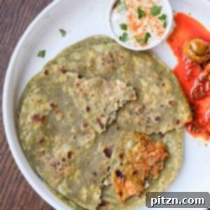 spinach paratha on a plate with raita and Indian pickle