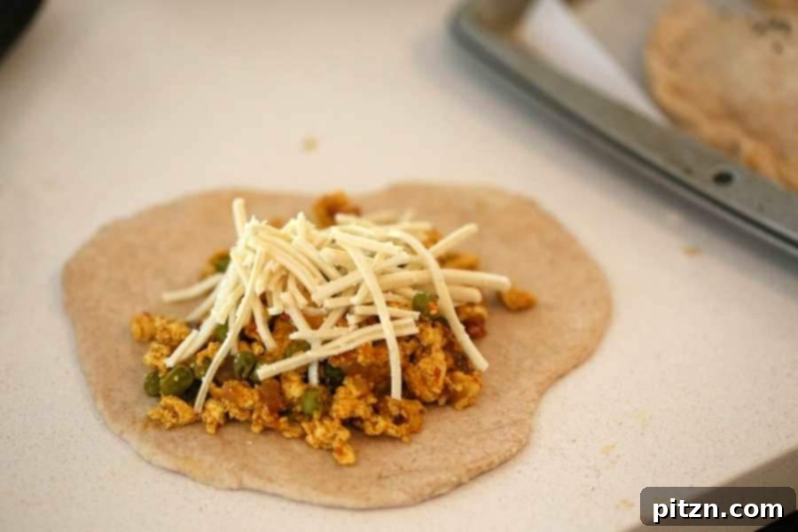 A hand rolling out vegan naan dough into a circular shape on a floured surface, preparing for filling.