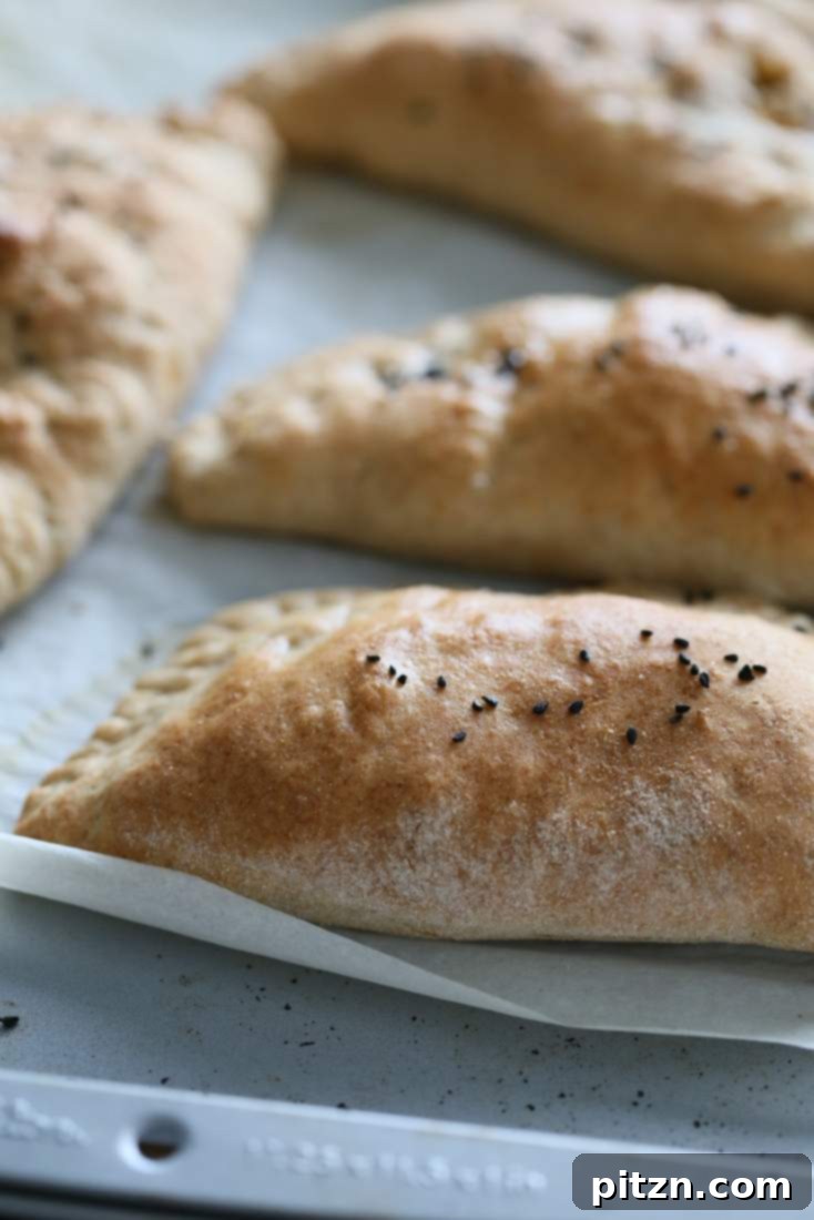 Vegan naan calzones sprayed with water and sprinkled with nigella seeds, resting before baking.