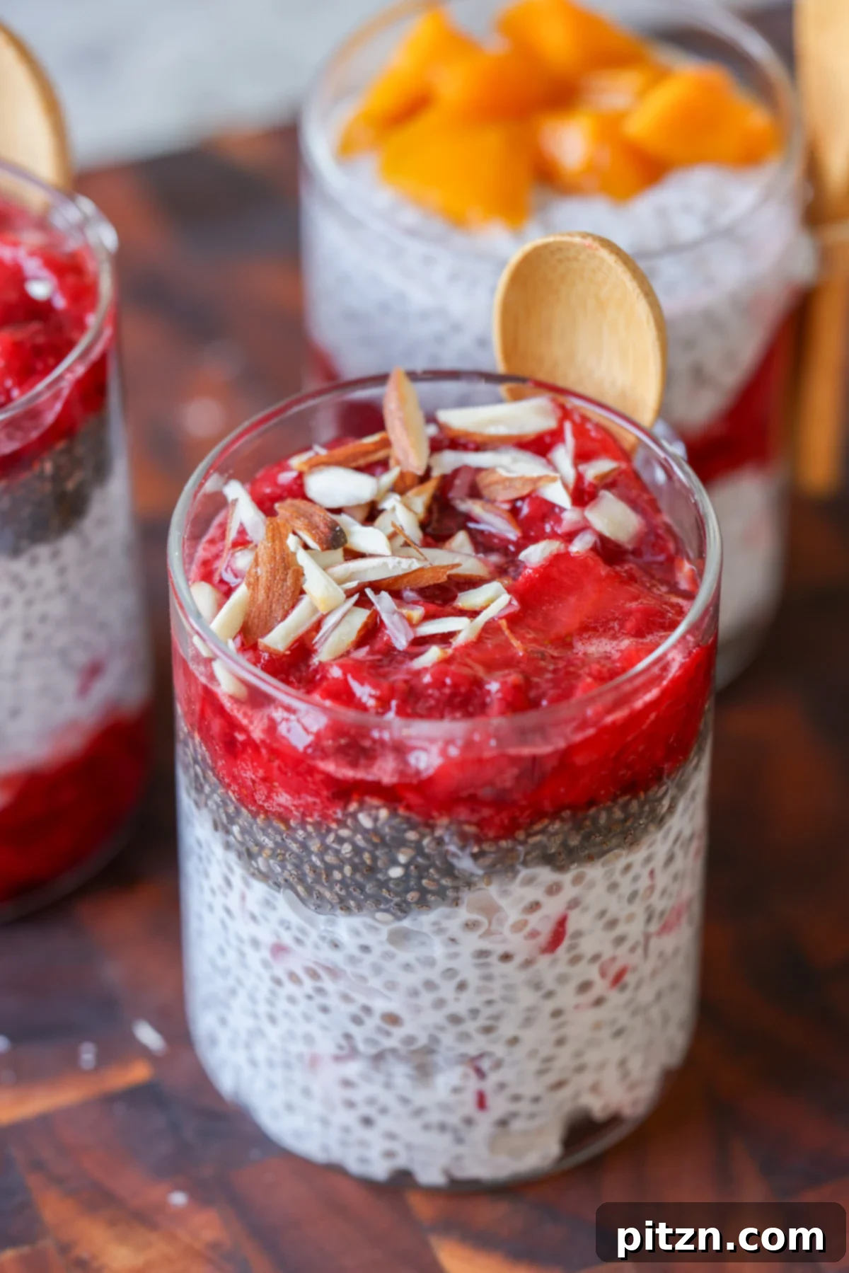 Strawberry chia pudding layered in a glass, topped with strawberry compote and slivered almonds.